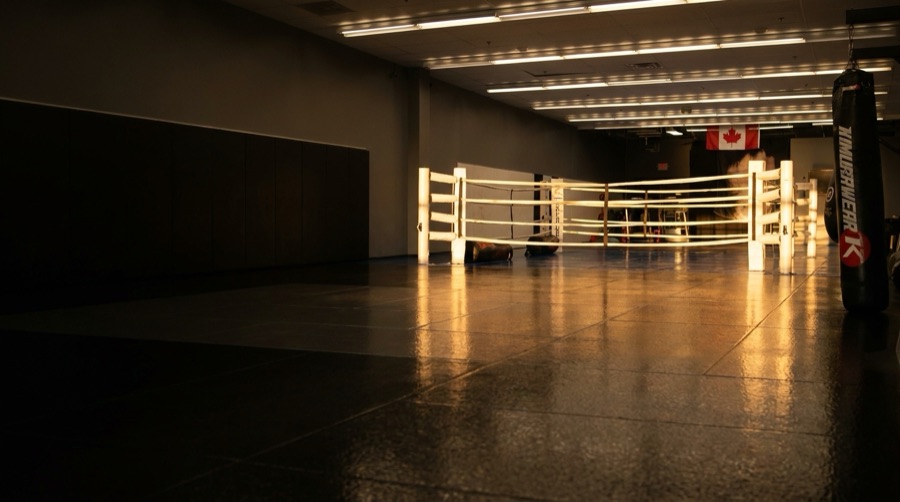The empty gym at Rumble Martial Arts at golden hour, black mats and the white boxing ring lit from the front windows.