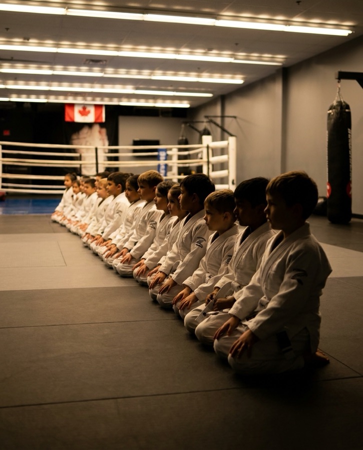 Young students in white gis kneeling in a line on the mats
